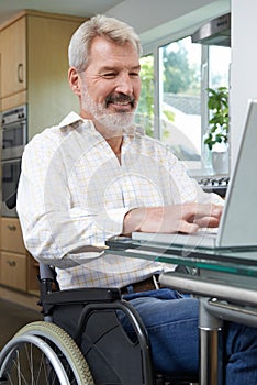 Disabled Man In Wheelchair Using Laptop At Home