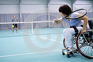 Disabled mature woman on wheelchair playing tennis on tennis court