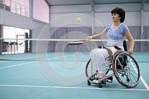 Disabled mature woman on wheelchair playing tennis on tennis court