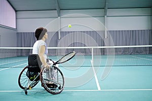 Disabled mature woman on wheelchair playing tennis on tennis court.