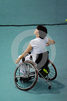 Disabled mature woman on wheelchair playing tennis on tennis court.