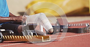 Disabled mixed race man with prosthetic legs sitting and putting his bandage on