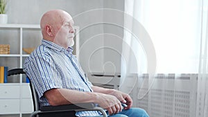 Disabled old man is sitting in a wheelchair at home alone. A handicapped person in a wheelchair is looking out the