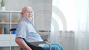 Disabled old man is sitting in a wheelchair at home alone. A handicapped person in a wheelchair is looking out the