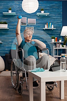 Disabled old woman in wheelchair raising arm training muscles resistance using dumbbells