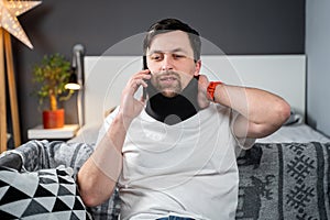 Disabled painful man with neck brace talking on phone at home. Man with spine trauma in neck brace cervical call