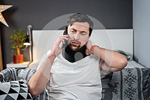 Disabled painful man with neck brace talking on phone at home. Man with spine trauma in neck brace cervical call