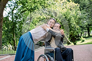 Disabled people, palliative care. Lifestyle summer portrait of senior bearded man in wheelchair hugging his young pretty