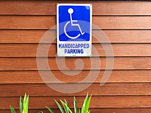 Disabled person parking sign on wooden wall. Blue sign `Handicapped parking`