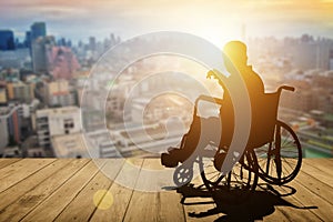 Disabled person silhouette with hand lift on wheelchair have sunset city background. International Disability Day or Handicapped