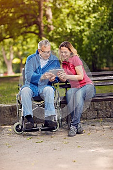 Disabled retiree man in park using tablet with daughter