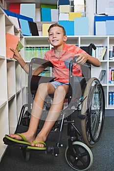 Disabled schoolboy selecting a book from bookshelf in library