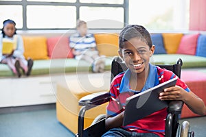 Disabled schoolboy on wheelchair using digital tablet in library