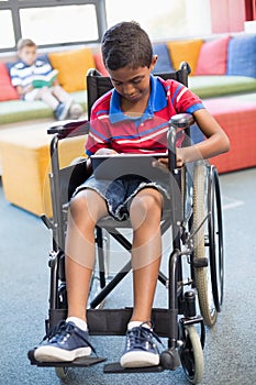 Disabled schoolboy on wheelchair using digital tablet in library