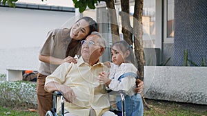 Disabled senior grandpa on wheelchair with grandchild and mother in park