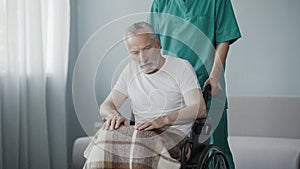 Disabled senior man sitting in wheelchair, male nurse supporting patient