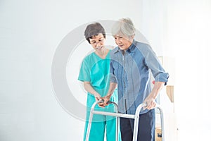 Disabled senior woman walking with assistance from nurse in hospital