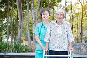 Disabled senior woman walking with assistance from nurse in park