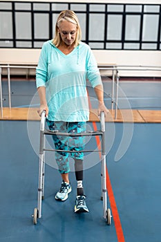 Disabled senior woman walking with walker in sports center