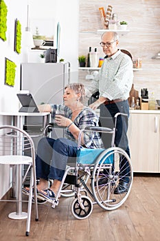 Disabled senior woman in wheelchair using tablet computer in kitchen
