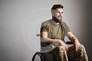 Disabled soldier sitting in a wheelchair and smiling on gray background