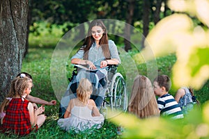 Disabled teacher conducts a lesson with children in nature. Interaction of a teacher in a wheelchair with students.