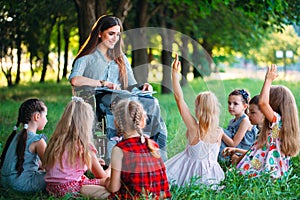 Disabled teacher conducts a lesson with children in nature. Interaction of a teacher in a wheelchair with students.