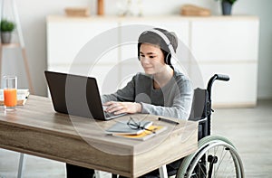 Disabled teen boy listening to music while doing online homework on laptop, indoors
