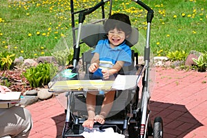 Disabled two year old boy having therapy in wheelchair outdoors