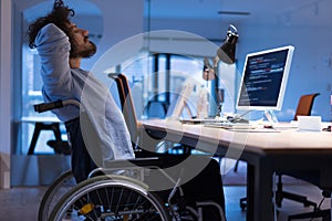Disabled web developer in the wheelchair works in the office at the computer while performing in co-working space. Disability and photo