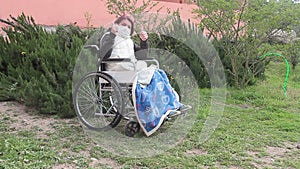 Disabled woman alone in a wheelchair with a protective mask that takes some air in the garden being in quarantine and makes the ok