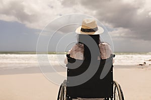 Disabled woman with hat sitting on wheelchair at beach
