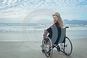 Disabled woman looking at camera sitting on wheelchair at beach