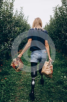 Disabled woman in prostheses carries two paper bag with apples.
