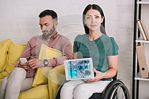 Disabled woman showing digital tablet with dna information app while sitting near boyfriend using smartphone