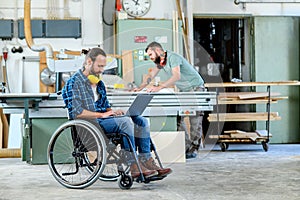 Worker in wheelchair in a carpenters workshop with his colleagu