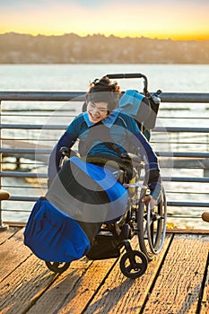 Disabled young boy in wheelchair by lake at sunset