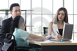 Disabled young female in wheelchair works in the modern office. Office workers are making a conversation