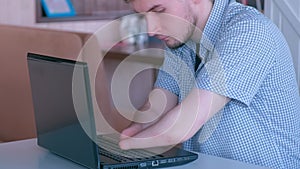 Disabled young man with amputated two stump hands in cafe works types on laptop.