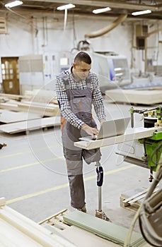 Disabled young man with artificial leg is working at the furniture factory