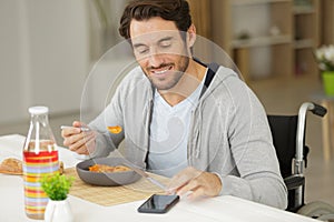 Disabled young man having lunch and using phone