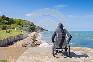 Disabled young man sitting in a wheelchair and looks at the sea