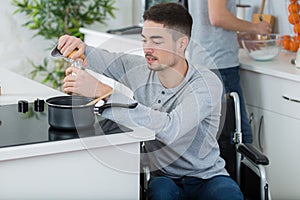 Disabled young man in wheelchair cooking in kitchen