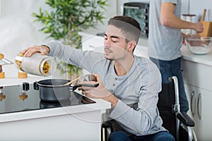 Disabled young man in wheelchair cooking meal in kitchen