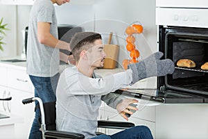 Disabled young man in wheelchair opens oven to prepare food