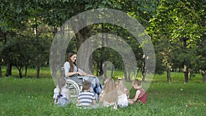 Disabled young teacher reading book to boys and girls in park