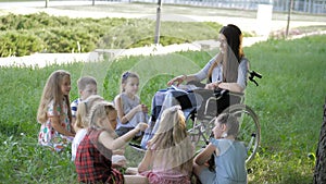 Disabled young teacher reading book to boys and girls in park