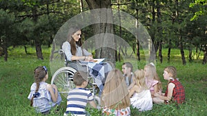 Disabled young teacher reading book to boys and girls in park