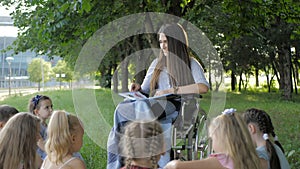 Disabled young teacher reading book to boys and girls in park