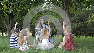 Disabled young teacher reading book to boys and girls in park